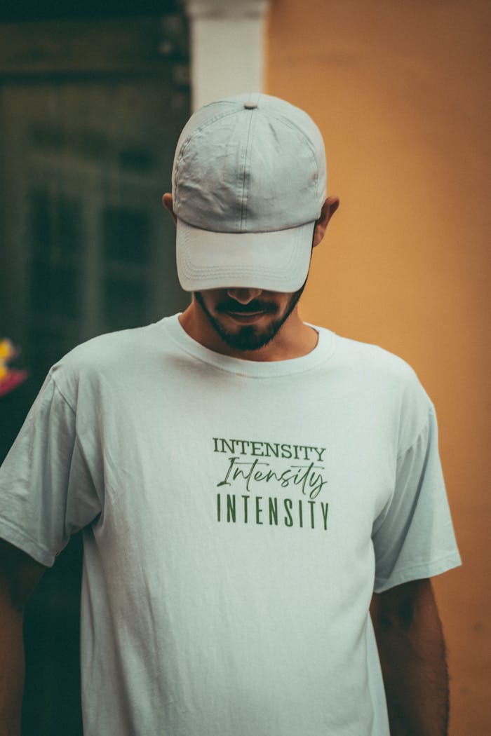 A man wearing a cap and shirt with the text 'Intensity' stands indoors, looking down thoughtfully.