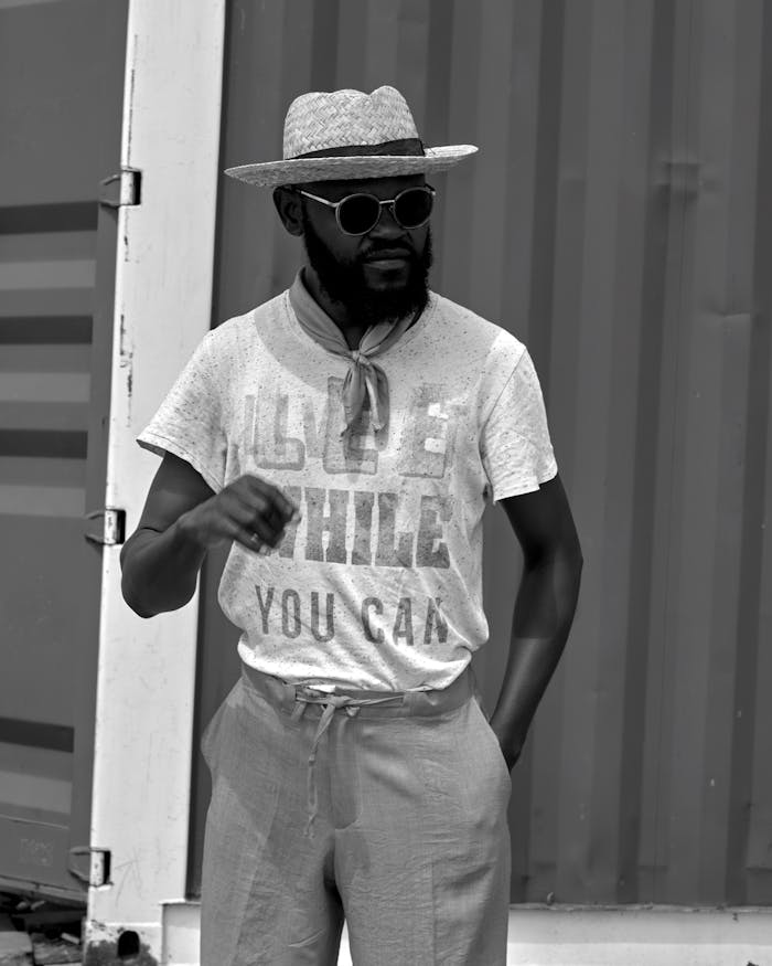 Black and white photo of a stylish man wearing sunglasses and a hat, exuding confidence.