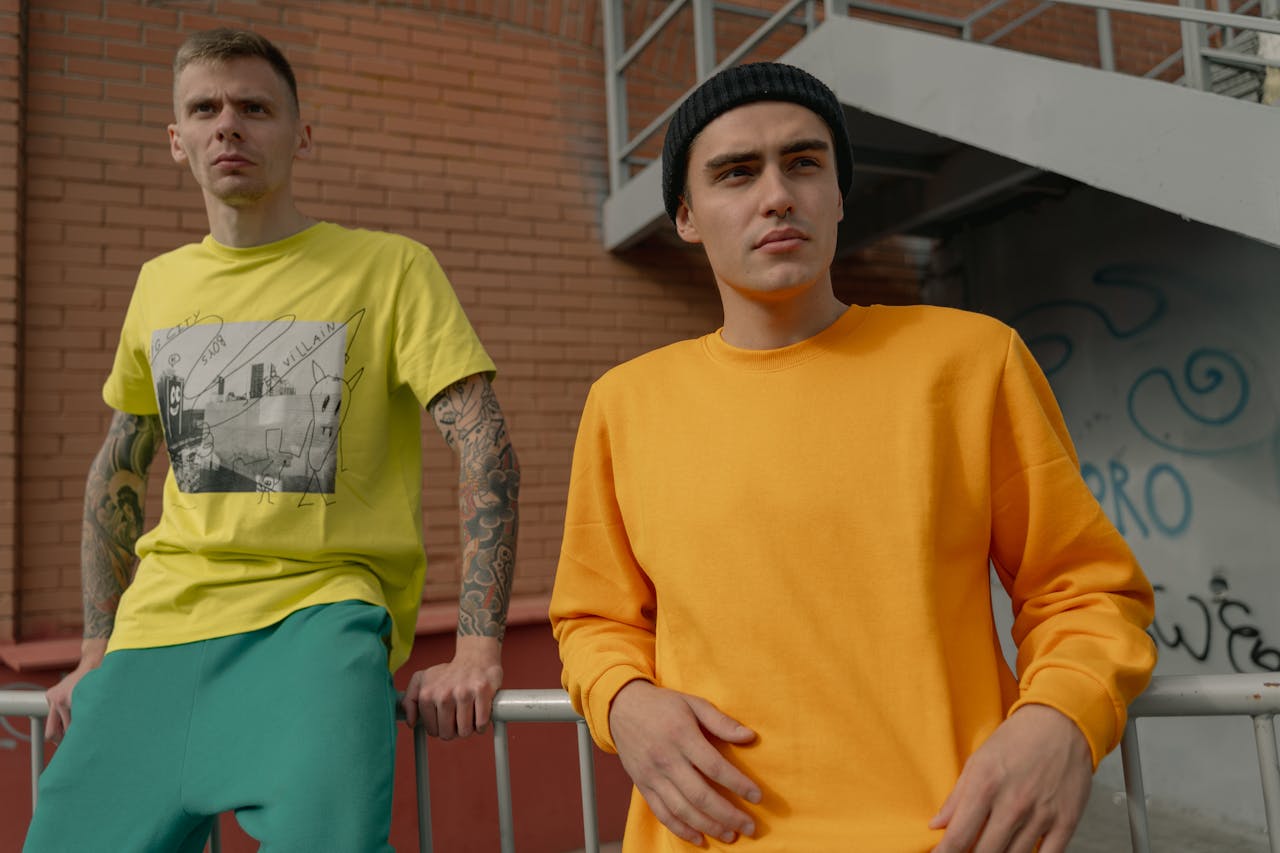 Two stylish young men in casual streetwear pose against an urban backdrop.