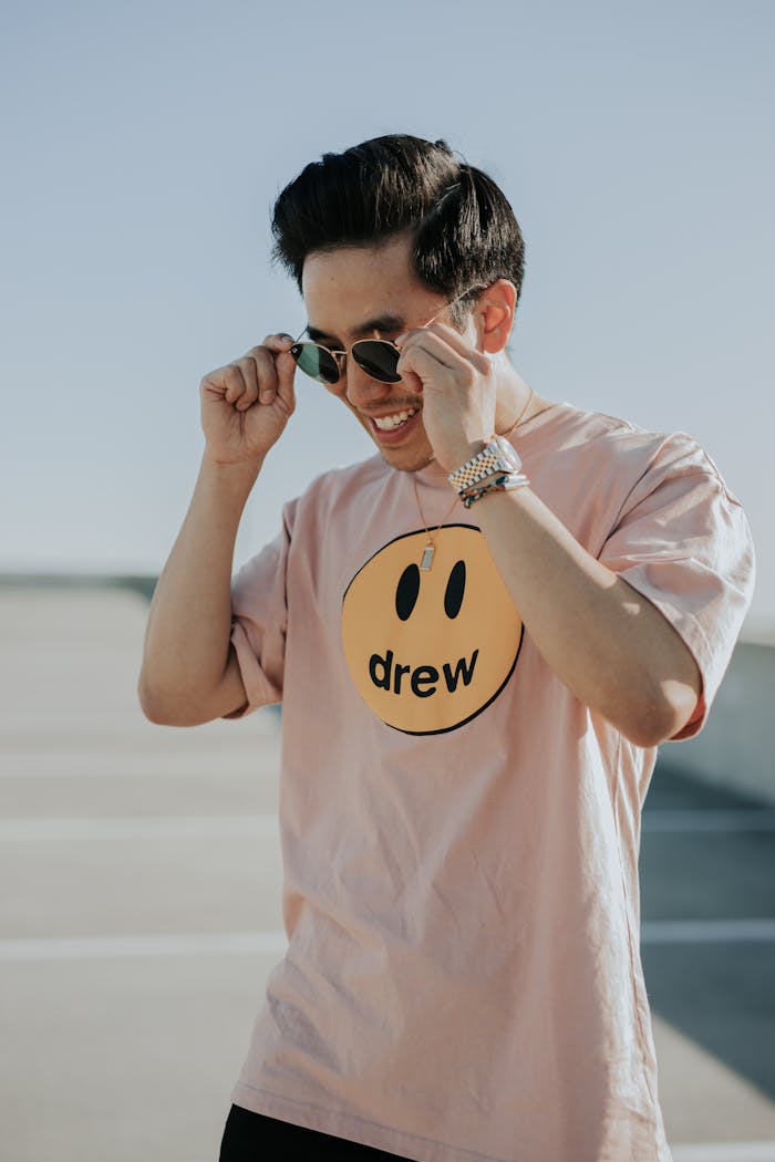 creative-02 Trendy young man smiling while adjusting sunglasses outdoors. Casual fashion style and youthful vibe.