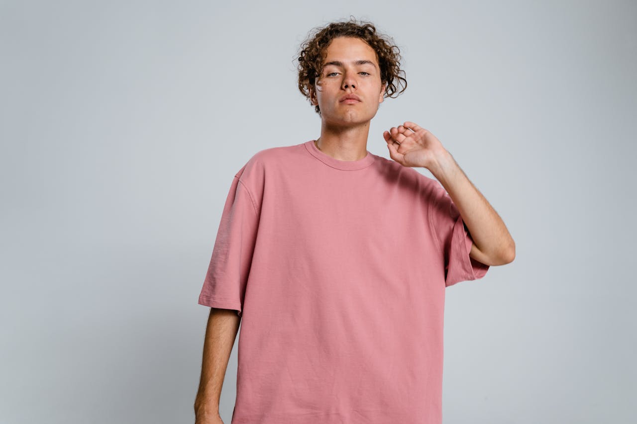 Stylish young man wearing a pink t-shirt posing in studio.